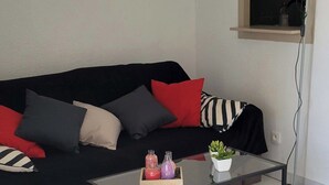 A living room with a black sofa, red and grey cushions, a glass coffee table with decorative items, a floor lamp, and a mirror on the wall.