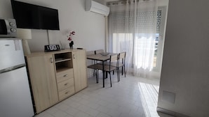 A compact kitchen with a microwave, refrigerator, wooden cabinet, and a dining table with chairs.