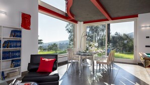 A modern living room with a black sofa, a dining table set for four, and a bookshelf filled with books. - Villa Dada 10, Emma Villas (Rosignano Marittimo)