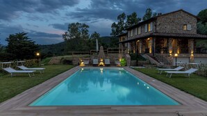 A rectangular pool with lounge chairs and a stone building with a balcony in the background. - Villa Dada 10, Emma Villas (Rosignano Marittimo)