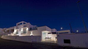 Un bâtiment moderne de couleur blanche, doté de nombreux balcons et d’un espace extérieur aménagé avec des sièges, protégé par un auvent.