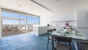 Una cocina moderna con una mesa de comedor de cristal, armarios blancos y vistas al exterior.
