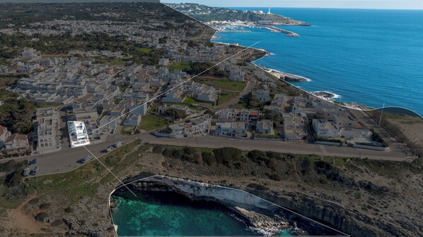 Vue aérienne d’une ville côtière, avec une falaise imposante, un port de plaisance et un phare visible au loin.