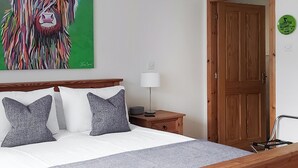 Une chambre à coucher avec un cadre de lit en bois, deux oreillers, une table de chevet avec une lampe et un mur vert orné d’un tableau représentant un lion.