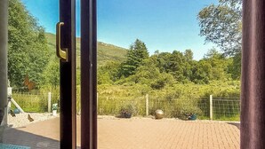 Un espace patio doté d’un sol en briques, d’une clôture en métal et offrant une vue sur un paysage verdoyant, avec des arbres et des collines.