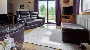 Un salon avec un canapé en cuir, une table basse, un téléviseur et une vue sur l’extérieur.