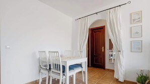 Un coin repas avec une table et des chaises blanches, un rideau et une porte en bois.