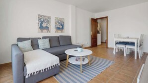 Un salon moderne avec un canapé gris, une petite table ronde et un coin repas comprenant une table et des chaises blanches.