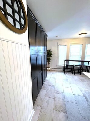 A kitchen with a dark wooden cabinet, a white radiator, a potted plant, and a dining area with a table and chairs. - Walk to everything! NEW Beautiful Home in Huron! (Huron)