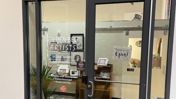 En glasklarlåse indgang til en bygning med et skilt der viser "Golden Belt Artists" og "Public Hours", angivende åbningstider.