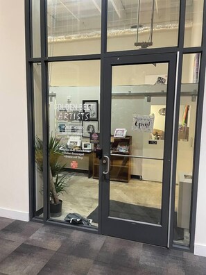 A glass door entrance to a building with a sign reading "Golden Belt Artists" and "Public Hours" indicating the business hours. - Durham Home for Corporate, Medical Stays, & Relos (Durham)