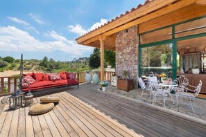 A wooden deck with a red sofa, white metal chairs, and a stone wall. - Agrology Lux (Rhodes)