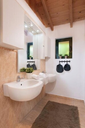 Un baño moderno con un lavamanos grande de color blanco, un espejo y una ventana pequeña con plantas.