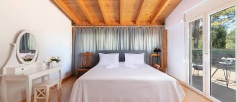 Ein Schlafzimmer mit Holzboden, einem Bett mit weißer Bettwäsche, einem Nachttisch, einem Spiegel und Blick durch eine Glastür.