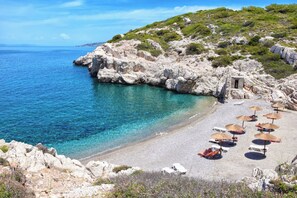 A coastal beach with rocky terrain, clear blue waters, and several sun loungers with umbrellas. - Agrology Lux (Rhodes)