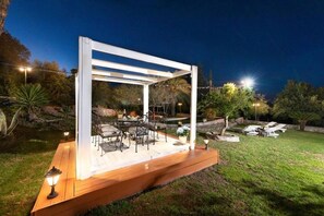 An outdoor patio with a wooden deck, white pergola, and tables with chairs. - Agrology Lux (Rhodes)