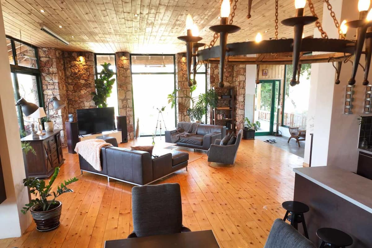 A spacious living room with a stone wall, wooden flooring, and a fireplace. There are multiple seating areas, including a sofa and armchairs, and a dining table with stools.