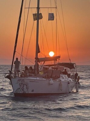 A sailboat with people on board, sailing on the water during sunset. - Agrology Lux (Rhodes)