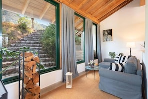 A room with a stone staircase outside, a grey sofa, a small table with a lamp, and a painting on the wall. - Agrology Lux (Rhodes)