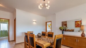 Ein Essbereich mit einem Holztisch und Stühlen, einer Chandelüster, einem Schrank mit Spiegel und einem Gemälde an der Wand.