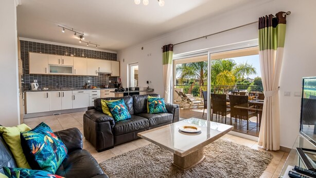 Ein modernes Wohnzimmer mit einem schwarzen Ledersofa, einem Glastisch und Blick auf die Terrassenanlage.