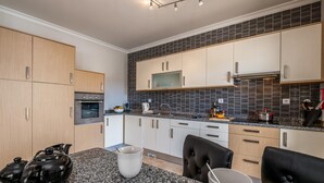 Eine moderne Küche mit Granit-Arbeitsplatten, einem eingebauten Backofen und einer Mikrowelle. Zwei schwarze Ledersessel und ein Granittisch sind ebenfalls vorhanden.