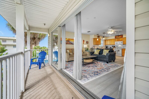 A covered porch with blue chairs, a sofa, and a patterned rug.
