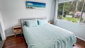 Relax in this serene bedroom with a large bed, nightstand, and framed beach scene above.