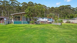 Stunning two-story house with a balcony and outdoor seating area, set amidst a lush lawn and surrounded by trees.