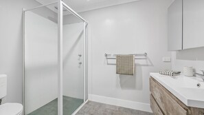Bathroom features a glass-enclosed shower, white toilet, and wooden vanity with a white countertop.