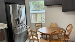 A modern kitchen with dark cabinets, stainless steel appliances, and a round wooden dining table with chairs.