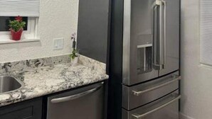 A modern kitchen with dark cabinets, a stainless steel refrigerator, and a marble countertop.