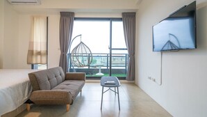 A hotel room with a bed, sofa, small table, TV, and a view of a building through the window. - YUTAI VILLA (Wujie)