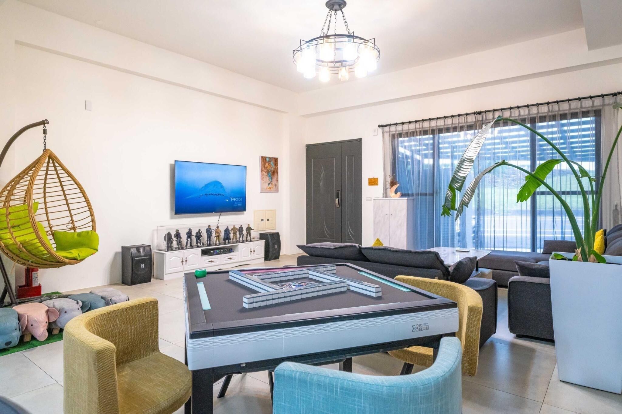 Una sala de estar moderna con un sofá, una silla colgante, un televisor y un ventanal con cortinas.