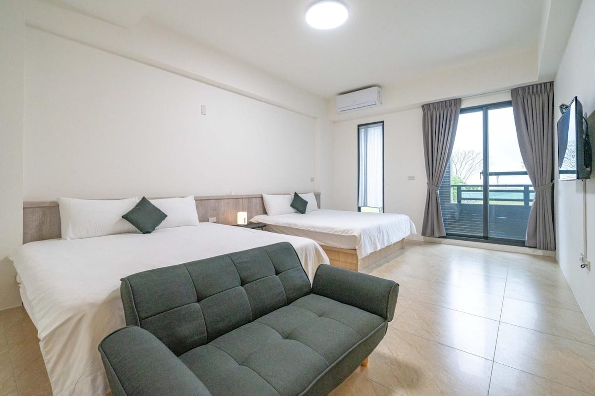 A hotel room with two beds, a sofa, and a balcony with curtains.