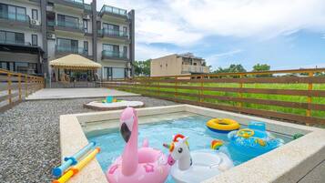 Una piscina con juguetes inflables, una cerca de madera y un edificio al fondo.
