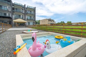 Piscina com brinquedos infláveis, cerca de madeira e um edifício ao fundo.