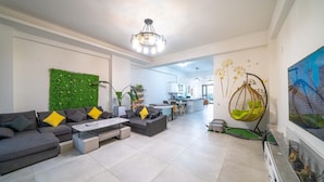 A modern living room with a sectional sofa, a coffee table, and a green wall. There is a kitchen in the background with white cabinets and a hanging chair. - YUTAI VILLA (Wujie)