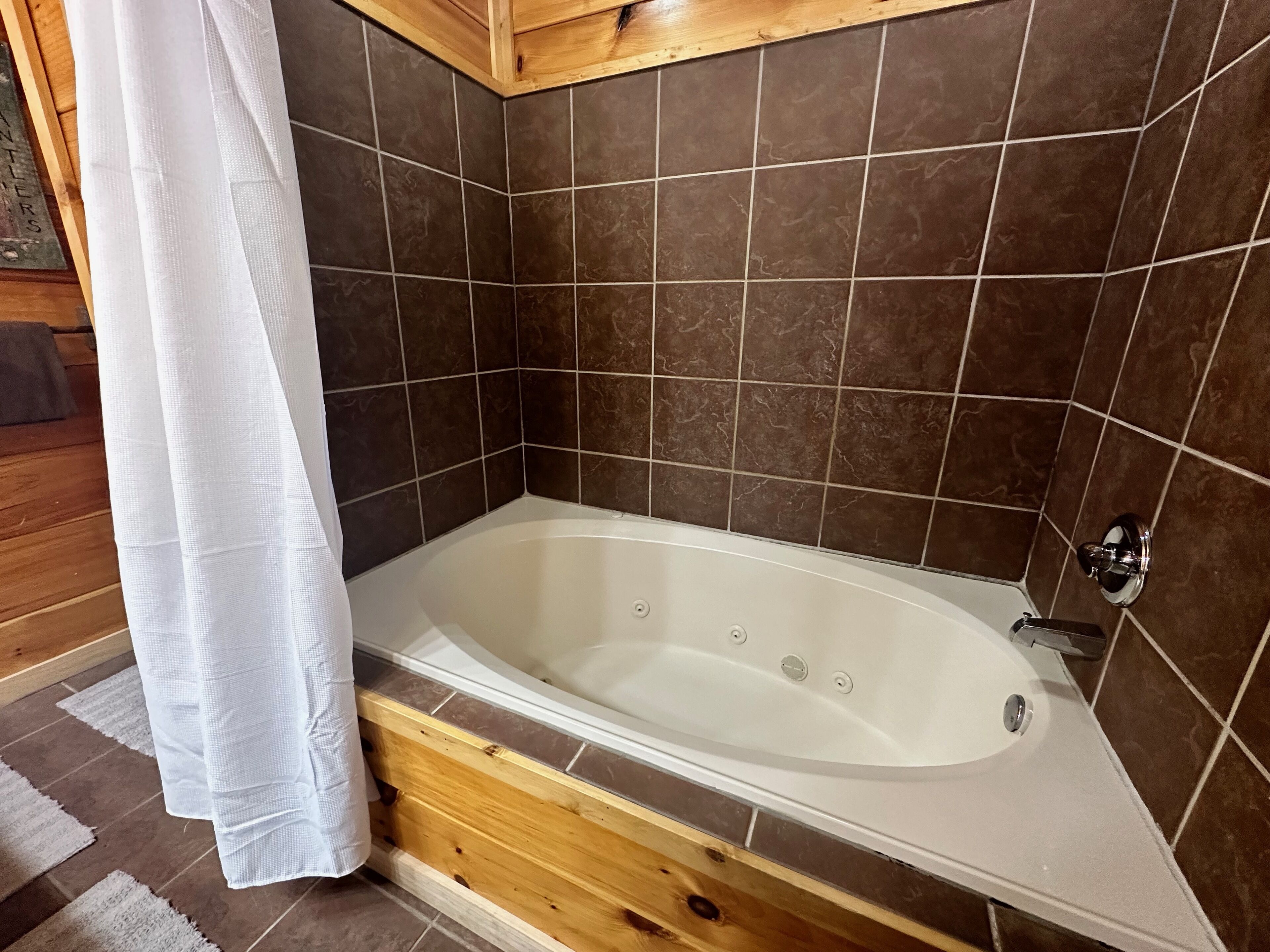 Une salle de bain moderne avec une baignoire sur pieds, des carreaux de couleur marron foncé et un plancher en bois.