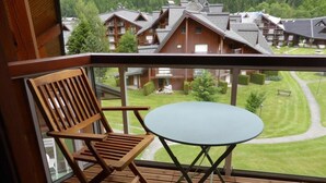 A balcony with a wooden chair and a small round table, overlooking a well-maintained lawn and several buildings in the background. - 200m from ski slopes, 3rd floor, balcony, parking, tv, ski locker, 23m², Les Contamines-Montjoie (Les Contamines-Montjoie)