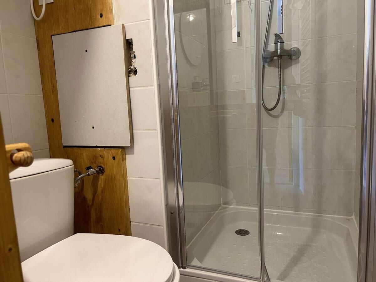 Un bagno con il water, un box doccia e un pannello di legno sopra il water.