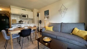 Uma sala de estar moderna com um sofá cinzento, almofadas amarelas, uma mesa de centro de madeira e uma área de jantar com uma mesa e cadeiras de madeira.