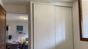 Um quarto com cama, armário, escrivaninha com cadeira e espaço de jantar com mesa e cadeiras.