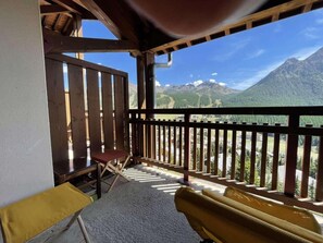 A balcony with a view of mountains, a wooden railing, and a red chair. - 4th floor, view mountain, terrace, tv, 33m², Montgenèvre (Montgenèvre)