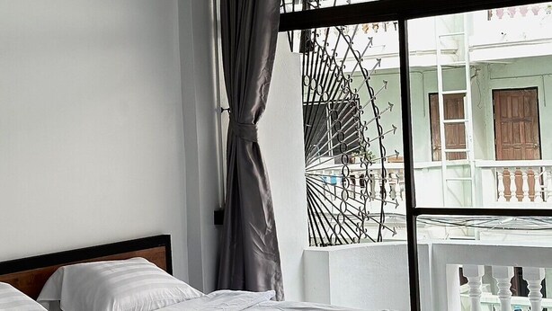 A modern hotel room with a large window, a bed with white linens, and a view of the outside balcony. - Sleep Owl Jomtien (Pattaya)
