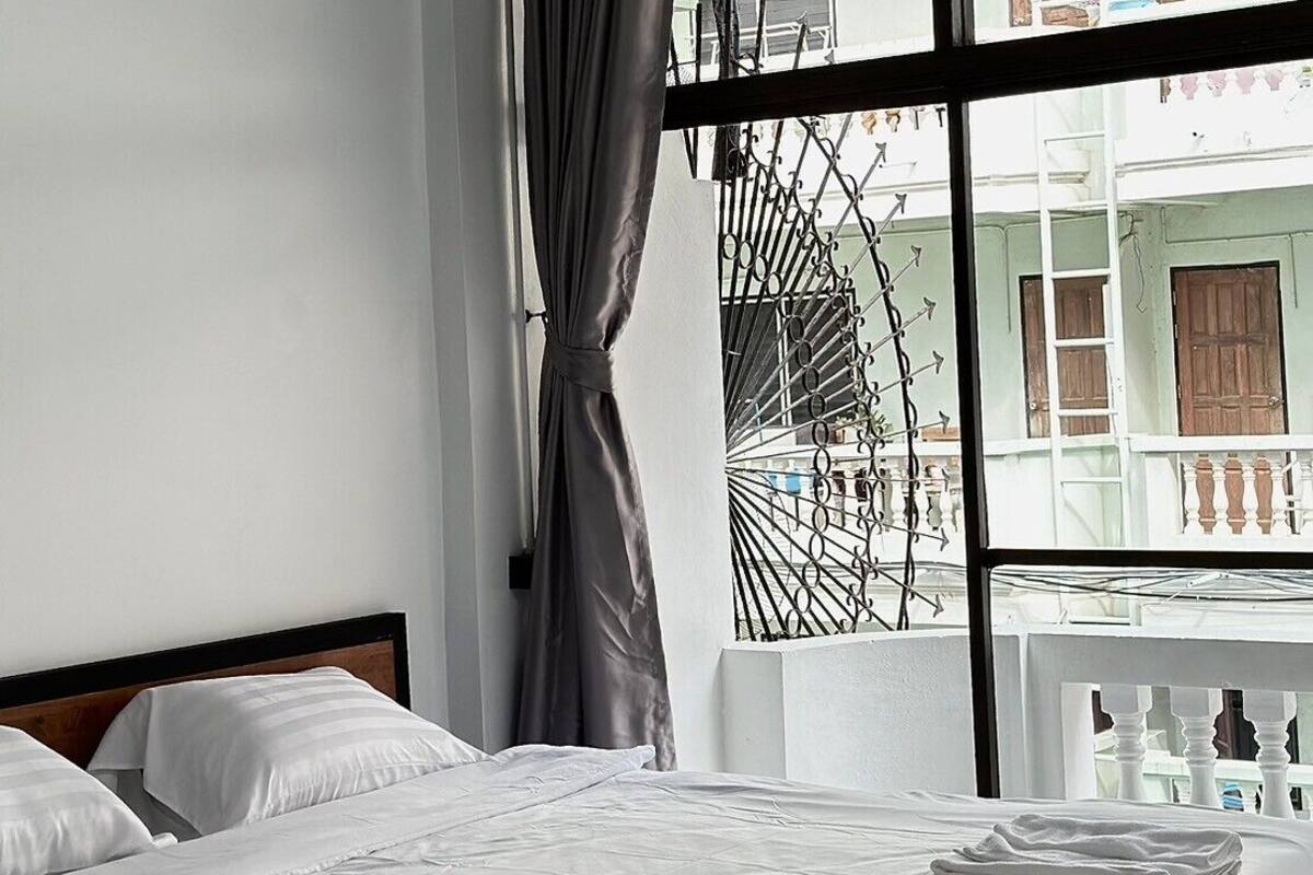 A modern hotel room with a large window, a bed with white linens, and a view of the outside balcony.