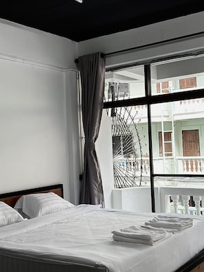 Ett modernt hotellrum med ett stort fönster, en säng med vita sängkläder och utsikt över balkongen.