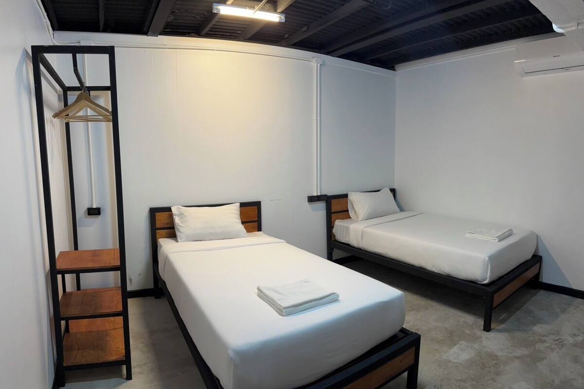 A room with two single beds, a wooden ladder, and a hanging garment rack.