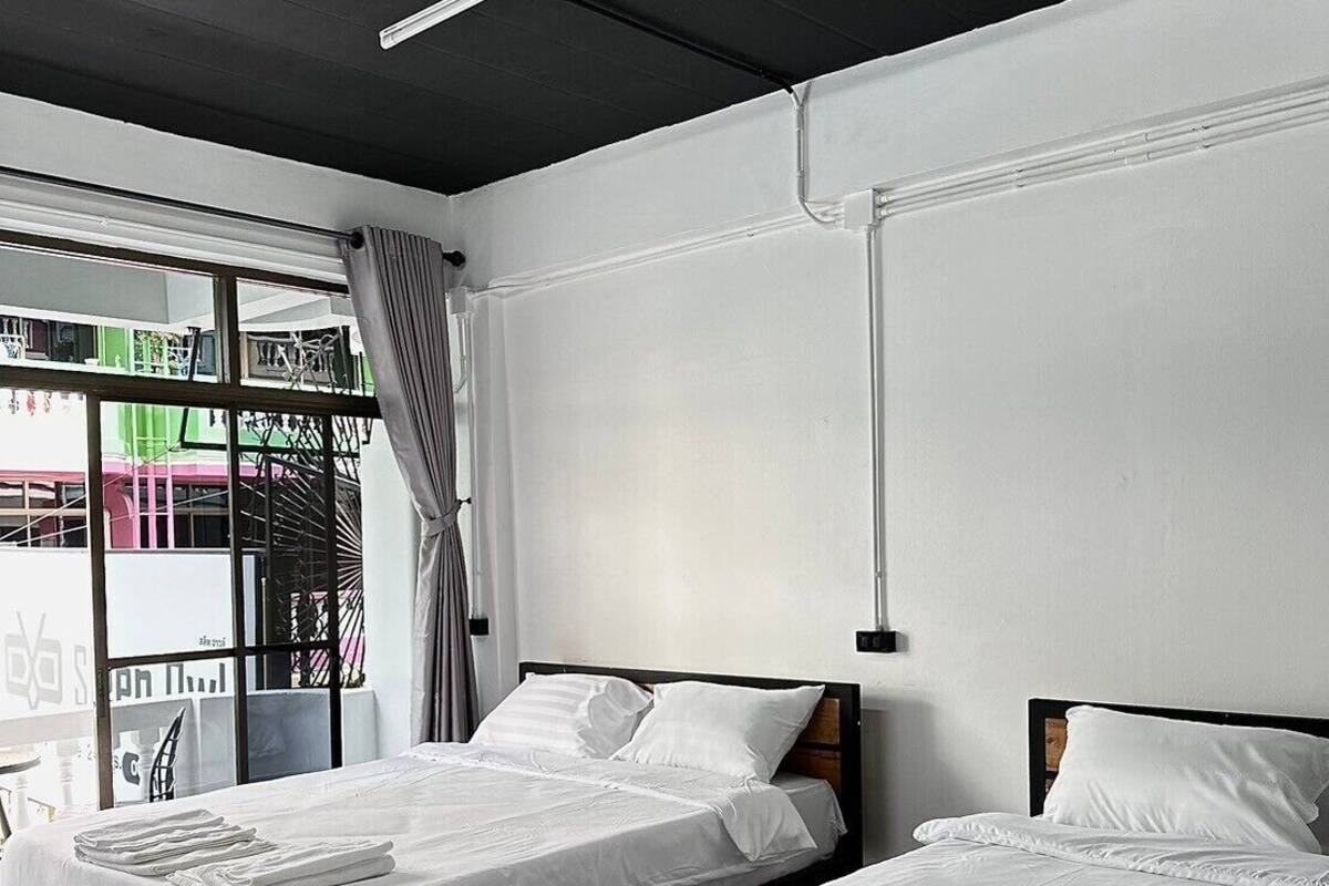 A modern hotel room with two beds, large windows, and a view of the outside.