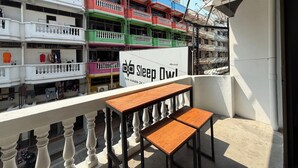 A balcony with a wooden table and chairs, a sign for 'Sleep Owl' indicating room availability, and multi-colored balconies of a building. - Sleep Owl Jomtien (Pattaya)
